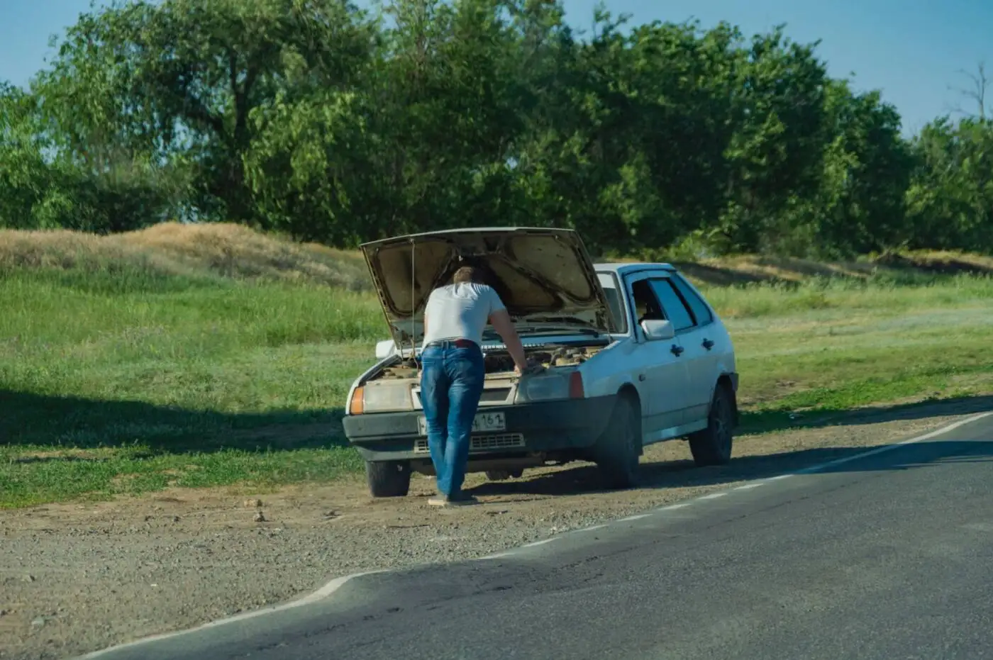 Person checking under the hood of a broken-down car on the roadside
